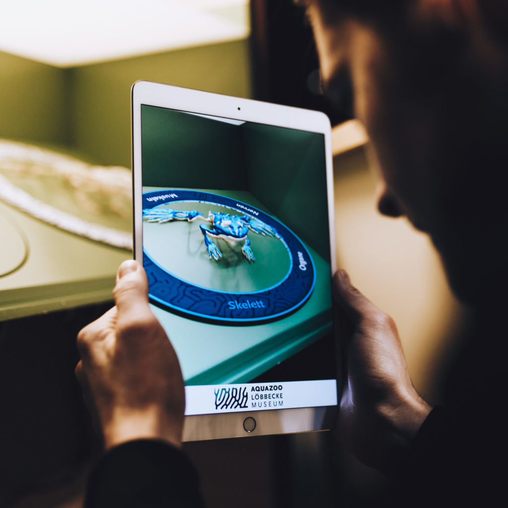 Visitor holding an iPad showing the AR frog skeleton inside the anatomy selector ring